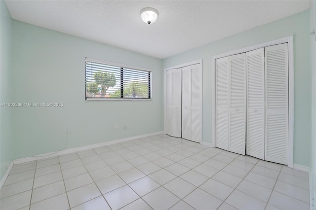 14431 SW 111th Ter, Miami, FL 33186 - unfurnished bedroom featuring two closets, baseboards, a textured ceiling, and light tile patterned floors