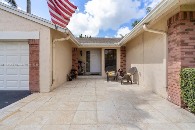 entrance to property with an attached garage, stucco siding, brick siding, and a patio