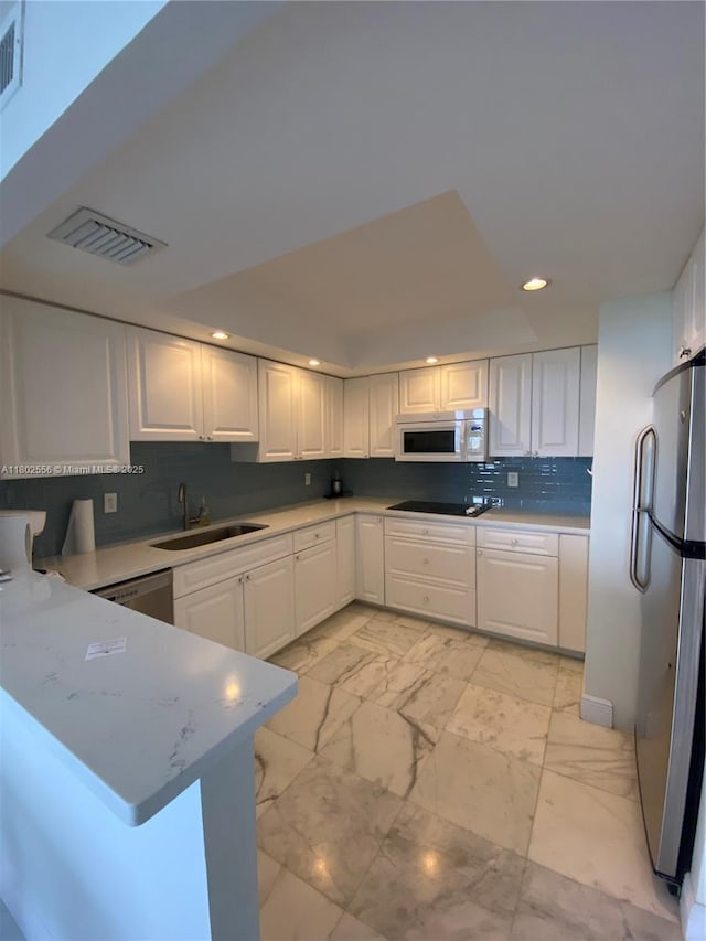 kitchen featuring a sink, freestanding refrigerator, white microwave, black electric cooktop, and recessed lighting
