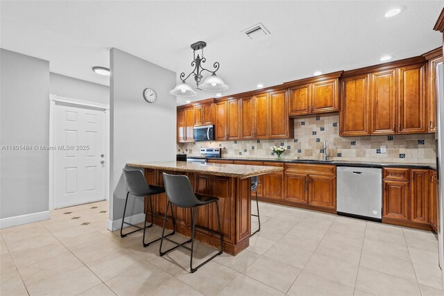 2426 NW 91st Ave, Coral Springs, FL 33065 - kitchen featuring stainless steel appliances, brown cabinetry, a kitchen breakfast bar, tasteful backsplash, and recessed lighting