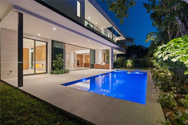 pool at night with a patio area and an outdoor pool
