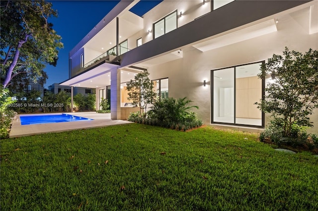 back of house at night with stucco siding and a lawn