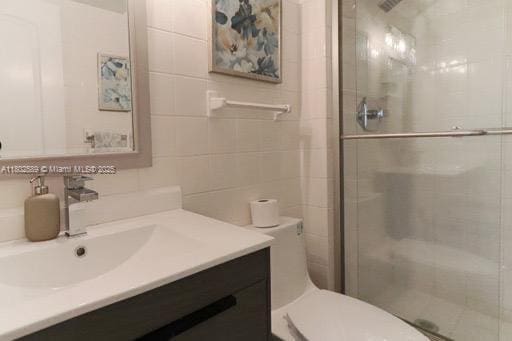 581 Blue Heron Dr Unit 318-B, Hallandale Beach, FL 33009 - bathroom featuring a stall shower, vanity, toilet, and tile walls