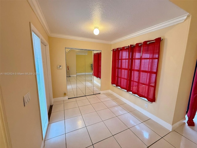 spare room with a textured ceiling, ornamental molding, light tile patterned flooring, and baseboards