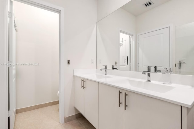 bathroom with toilet, baseboards, double vanity, and tile patterned floors