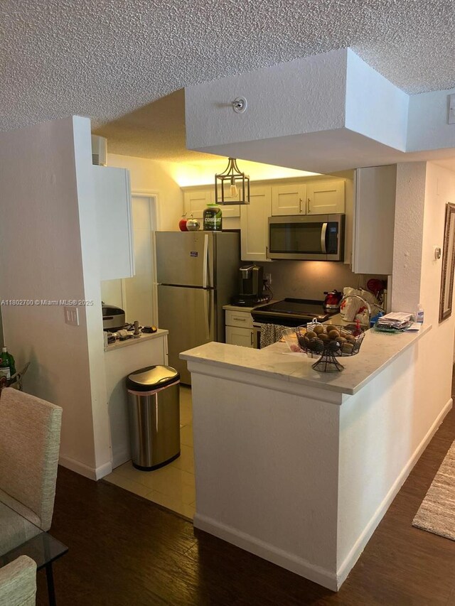 1610 NW 128th Dr Unit 104, Sunrise, FL 33323 - kitchen featuring stainless steel appliances, a textured ceiling, a peninsula, wood finished floors, and white cabinetry