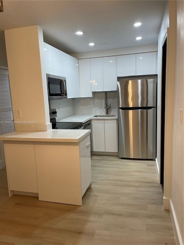 kitchen with stainless steel appliances, a sink, modern cabinets, white cabinetry, and a peninsula