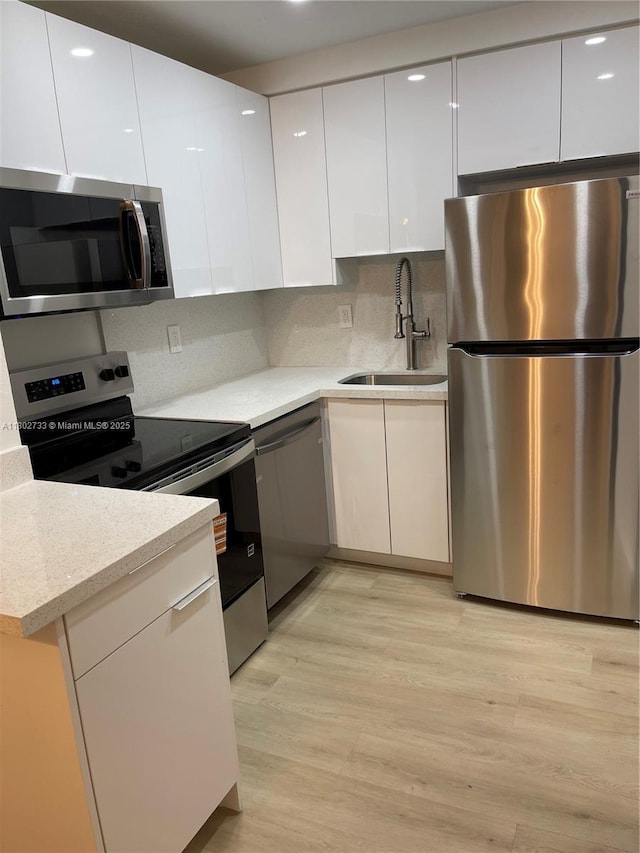 kitchen featuring appliances with stainless steel finishes, a sink, modern cabinets, white cabinets, and recessed lighting
