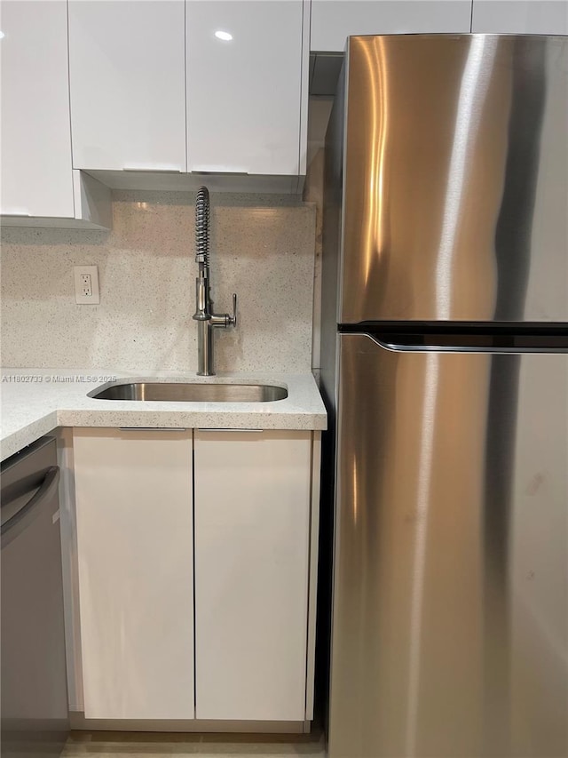 kitchen with appliances with stainless steel finishes, a sink, white cabinetry, modern cabinets, and tasteful backsplash