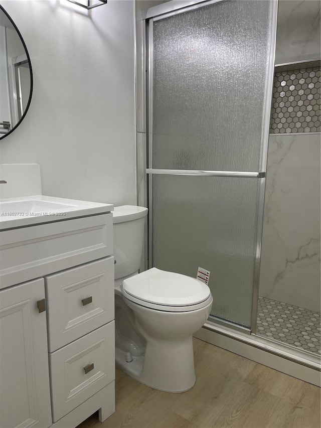 bathroom featuring wood finished floors, a stall shower, toilet, and vanity