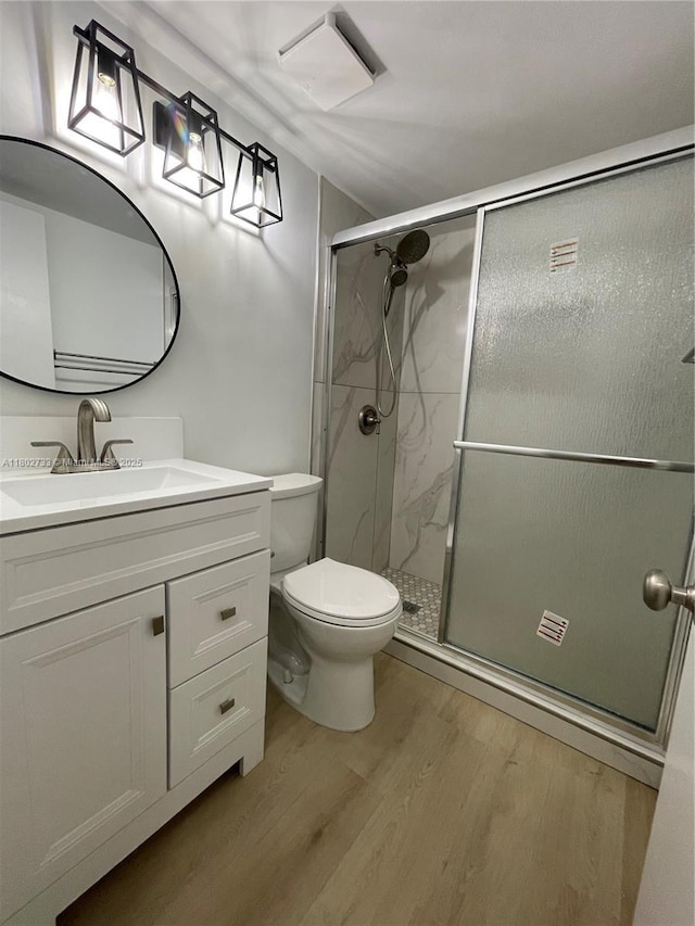 bathroom with wood finished floors, a stall shower, toilet, and vanity
