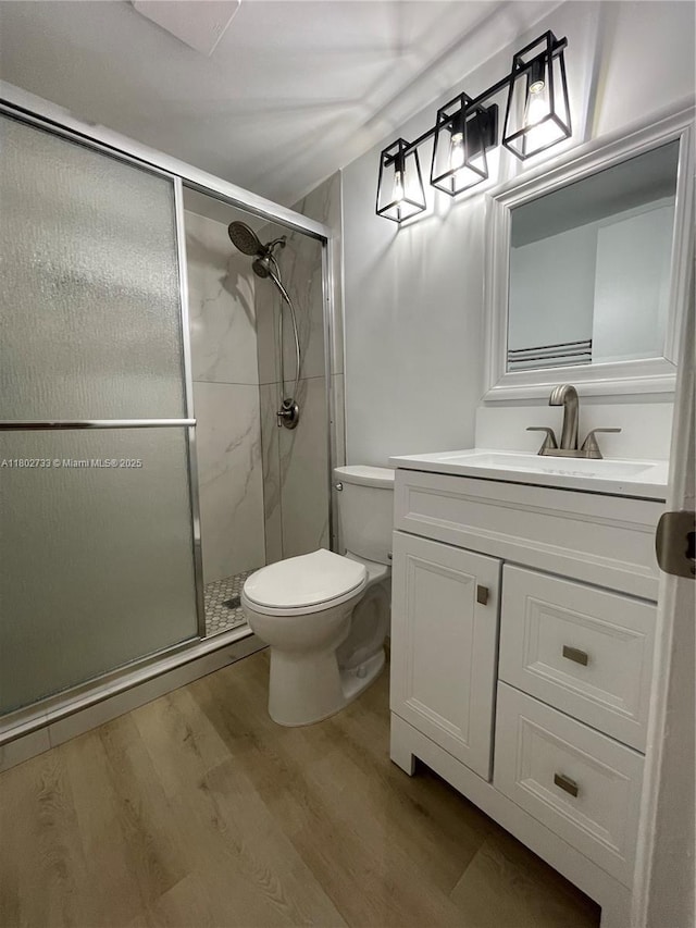 bathroom with wood finished floors, toilet, a shower stall, and vanity