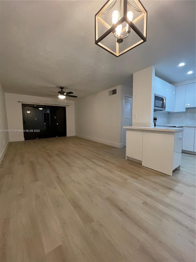 unfurnished living room with baseboards, light wood-style floors, ceiling fan, a chandelier, and recessed lighting