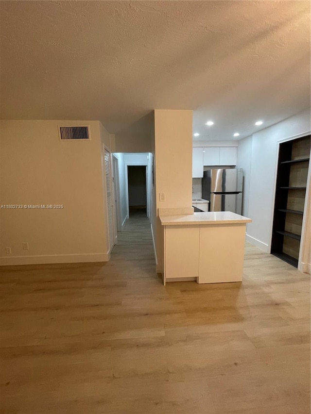 kitchen featuring freestanding refrigerator, light wood-style floors, a textured ceiling, baseboards, and a peninsula