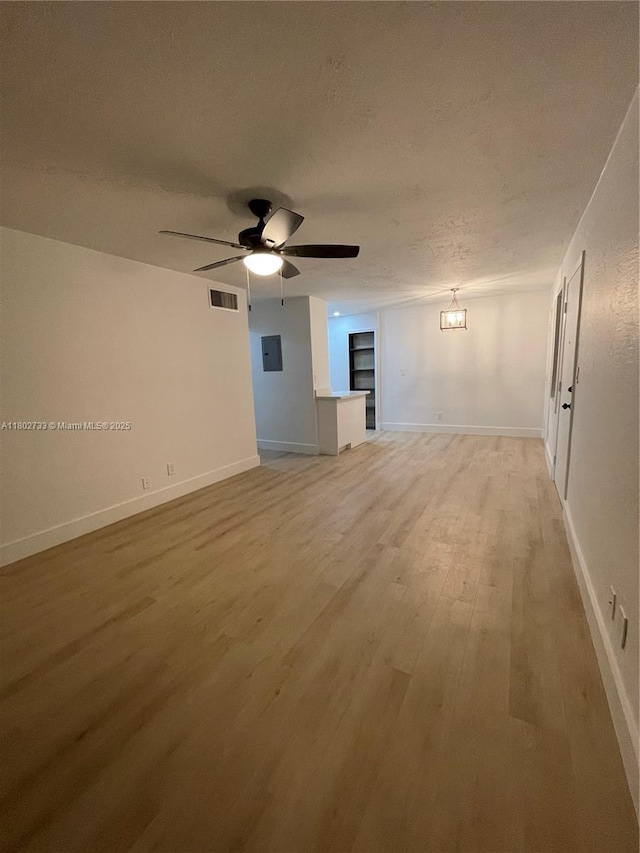 unfurnished room with a textured ceiling, light wood-style floors, a ceiling fan, and baseboards