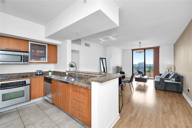 888 S Douglas Rd Unit 910, Coral Gables, FL 33134 - kitchen featuring appliances with stainless steel finishes, a peninsula, open floor plan, brown cabinetry, and dark stone counters
