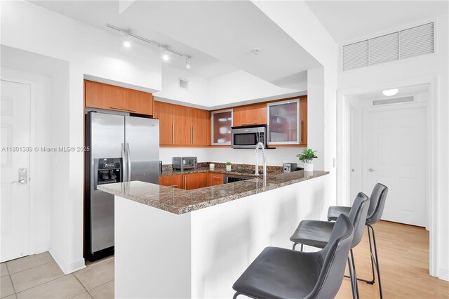 888 S Douglas Rd Unit 910, Coral Gables, FL 33134 - kitchen featuring stainless steel appliances, brown cabinetry, a peninsula, glass insert cabinets, and dark stone countertops