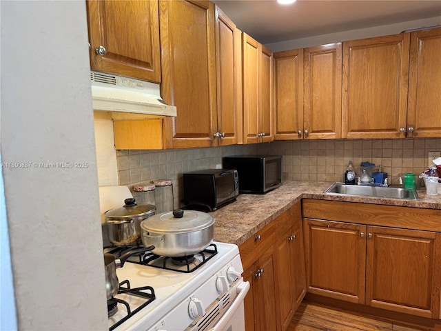 2175 NE 170th St Unit 202, North Miami Beach, FL 33162 - kitchen with under cabinet range hood, white gas range oven, tasteful backsplash, and brown cabinets