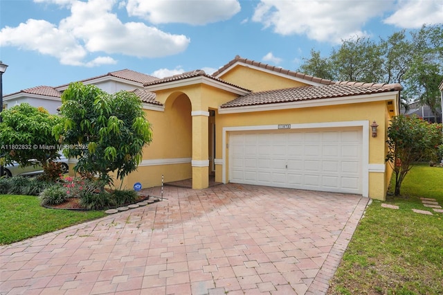 mediterranean / spanish home featuring decorative driveway, stucco siding, a garage, and a front lawn