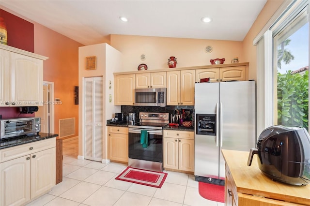 kitchen featuring appliances with stainless steel finishes, lofted ceiling, tasteful backsplash, light brown cabinetry, and light tile patterned flooring