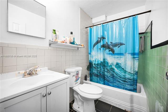 3446 NW 1st Ave, Miami, FL 33127 - full bathroom with tile walls, tile patterned floors, shower / bath combo with shower curtain, toilet, and vanity