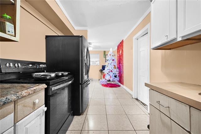 3446 NW 1st Ave, Miami, FL 33127 - kitchen with black appliances, white cabinetry, crown molding, light tile patterned flooring, and baseboards