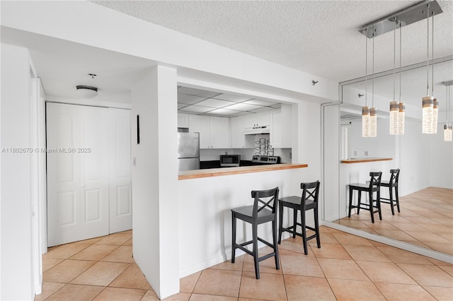 540 Brickell Key Dr Unit 904, Miami, FL 33131 - kitchen with under cabinet range hood, appliances with stainless steel finishes, light tile patterned floors, a kitchen bar, and white cabinets