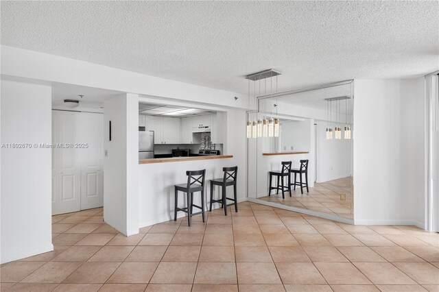 540 Brickell Key Dr Unit 904, Miami, FL 33131 - kitchen featuring freestanding refrigerator, a kitchen breakfast bar, light tile patterned flooring, a textured ceiling, and white cabinets