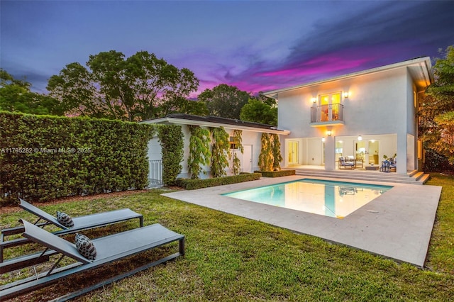 1415 Madrid St, Coral Gables, FL 33134 - back of house at dusk featuring a patio, a yard, an outdoor pool, stucco siding, and a balcony