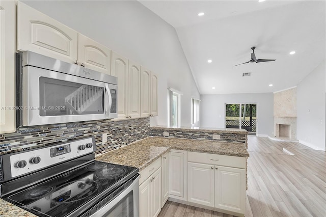 kitchen with appliances with stainless steel finishes, a peninsula, a fireplace, decorative backsplash, and light stone counters