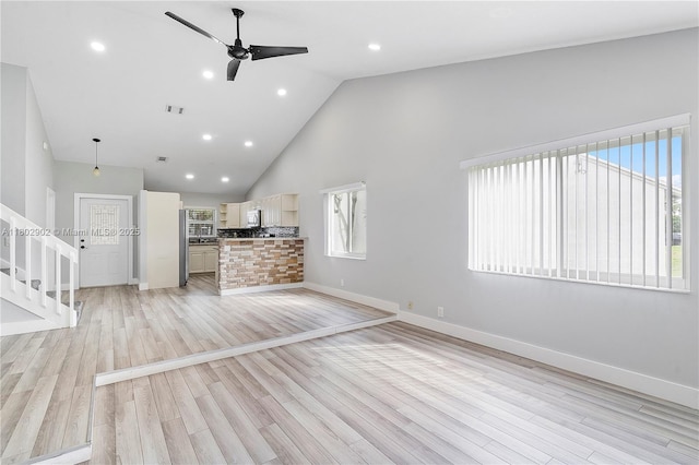 unfurnished living room with high vaulted ceiling, ceiling fan, baseboards, stairs, and light wood-style floors