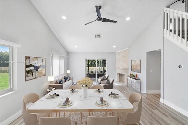 dining room with light wood-style floors, high vaulted ceiling, healthy amount of natural light, a ceiling fan, and baseboards
