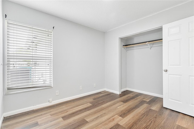 unfurnished bedroom featuring wood finished floors, a closet, and baseboards