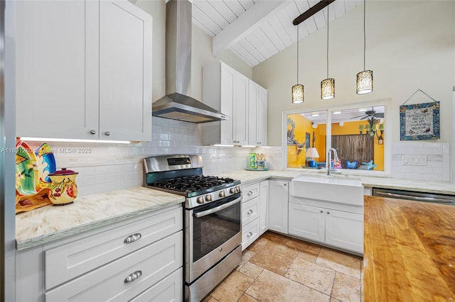 kitchen with stainless steel gas range, wall chimney exhaust hood, a sink, tasteful backsplash, and stone tile floors