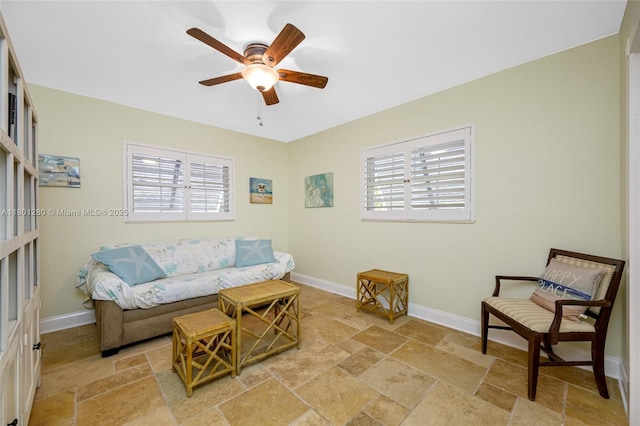 living area featuring stone tile flooring, plenty of natural light, a ceiling fan, and baseboards
