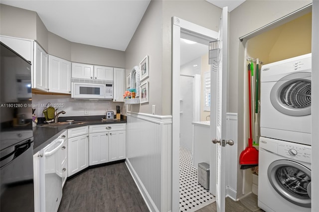laundry area with stacked washer and clothes dryer, a sink, dark wood-type flooring, and wainscoting