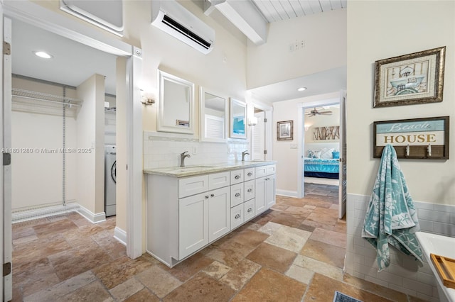 ensuite bathroom with a wall mounted AC, stone tile flooring, washer / dryer, a ceiling fan, and double vanity