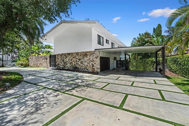 rear view of house with stone siding, stucco siding, driveway, and a garage