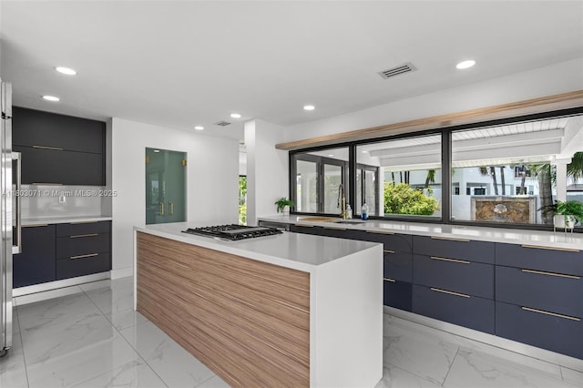 kitchen featuring modern cabinets, stainless steel gas cooktop, light marble finish floors, a kitchen island, and recessed lighting