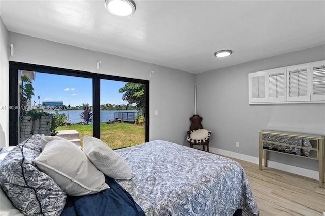 bedroom featuring access to exterior, a water view, light wood finished floors, and baseboards