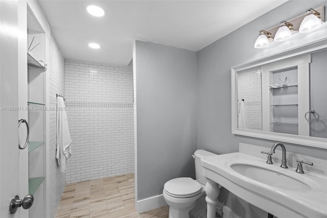 bathroom with a tile shower, a sink, toilet, and recessed lighting