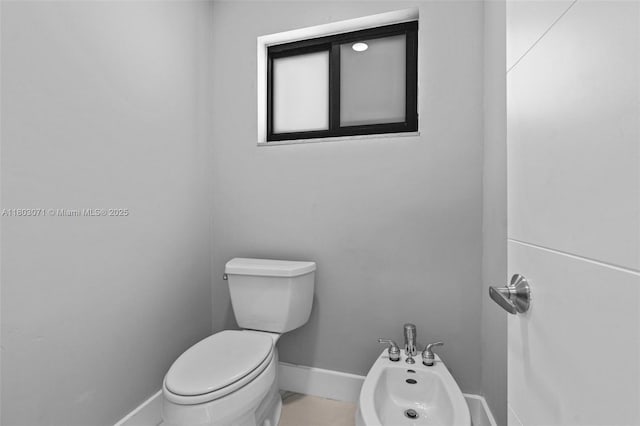 bathroom with baseboards, a bidet, and toilet