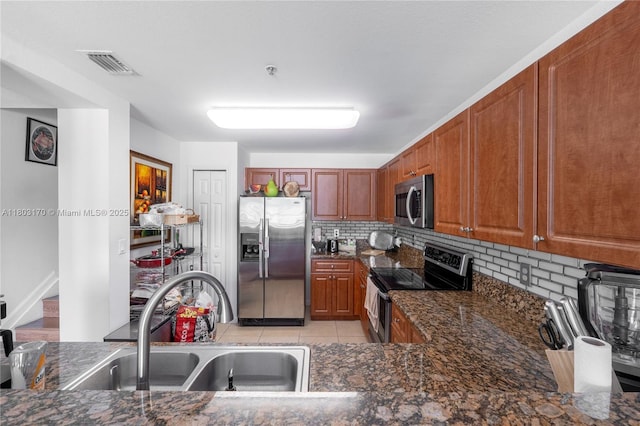 kitchen with stainless steel appliances, tasteful backsplash, light tile patterned flooring, dark stone countertops, and brown cabinetry