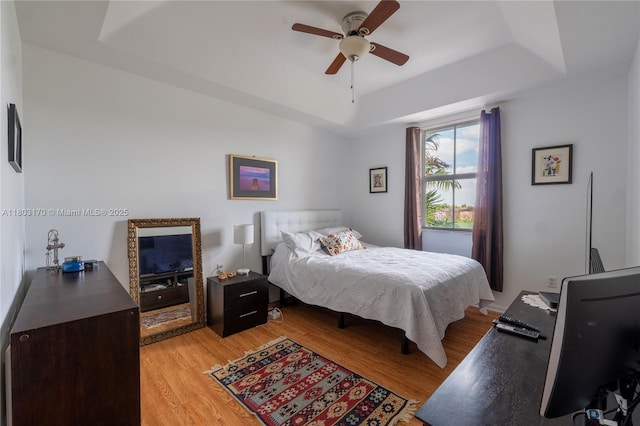 bedroom featuring a raised ceiling, light wood-style flooring, and a ceiling fan