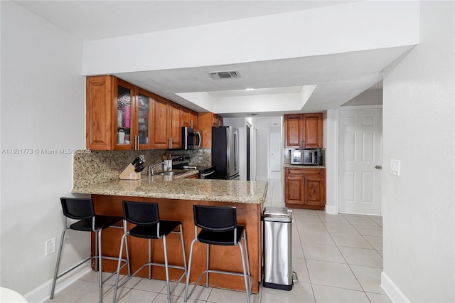 857 W 37th St, Hialeah, FL 33012 - kitchen with stainless steel appliances, a tray ceiling, brown cabinets, and a peninsula