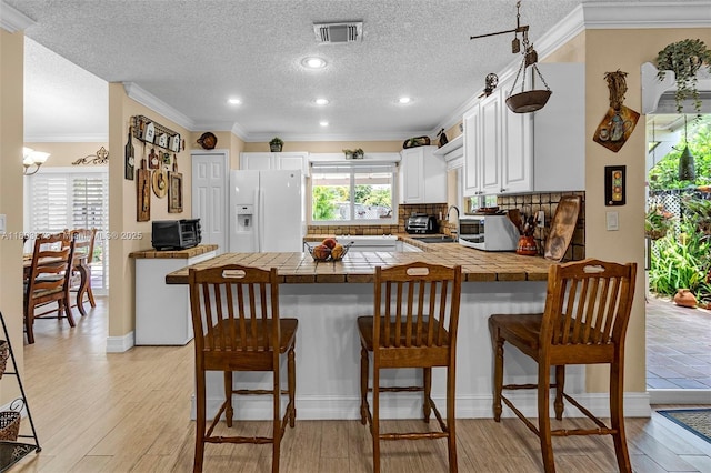 13338 SW 8th Ln, Miami, FL 33184 - kitchen with white refrigerator with ice dispenser, a peninsula, white cabinetry, ornamental molding, and light wood finished floors