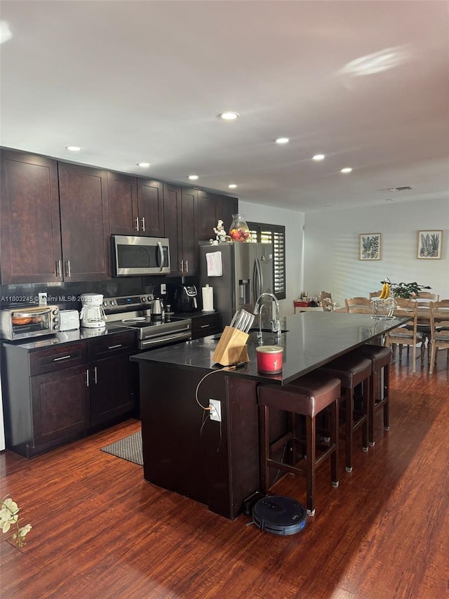 111 SW 24th Ave, Miami, FL 33135 - kitchen with appliances with stainless steel finishes, a kitchen breakfast bar, dark countertops, a center island with sink, and dark wood-style flooring