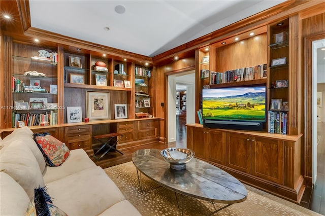living area featuring wood finished floors, vaulted ceiling, built in shelves, and a desk