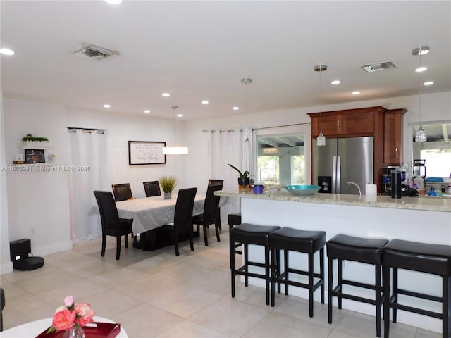 kitchen with stainless steel refrigerator with ice dispenser, recessed lighting, a breakfast bar area, pendant lighting, and light tile patterned flooring