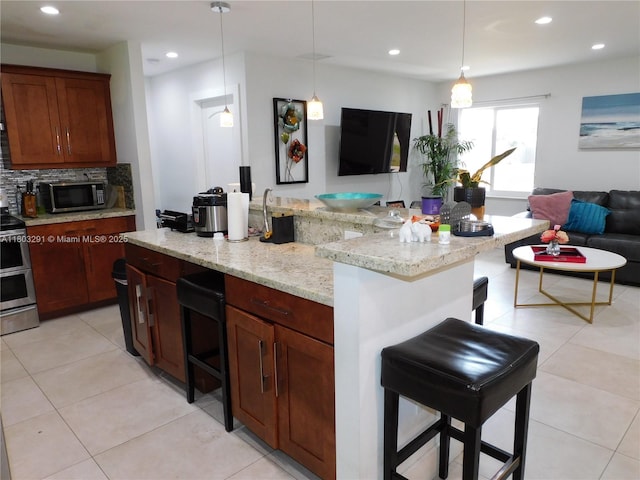 kitchen featuring appliances with stainless steel finishes, open floor plan, a kitchen breakfast bar, recessed lighting, and light stone counters